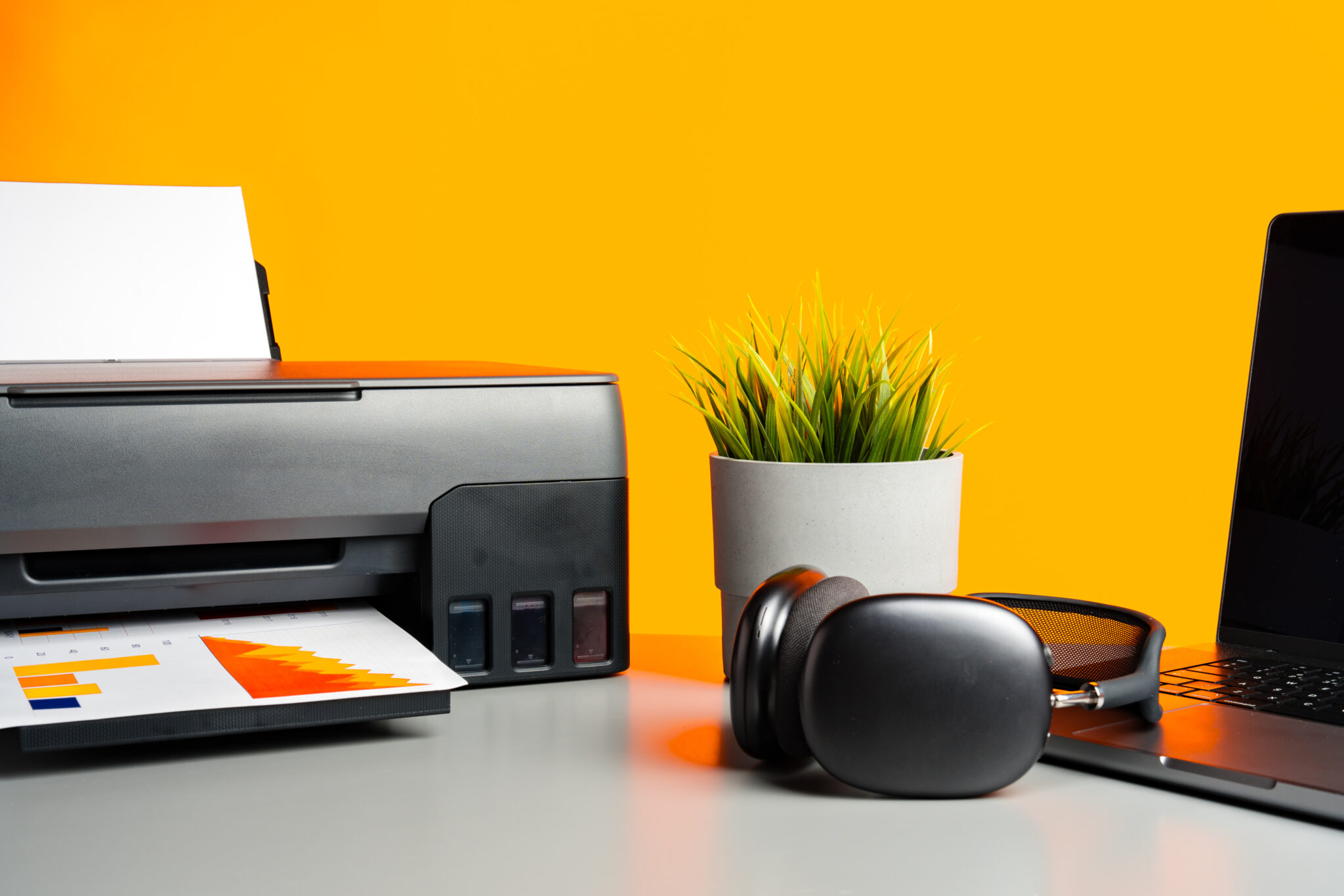 Laser printer and laptop on desk against yellow background close up